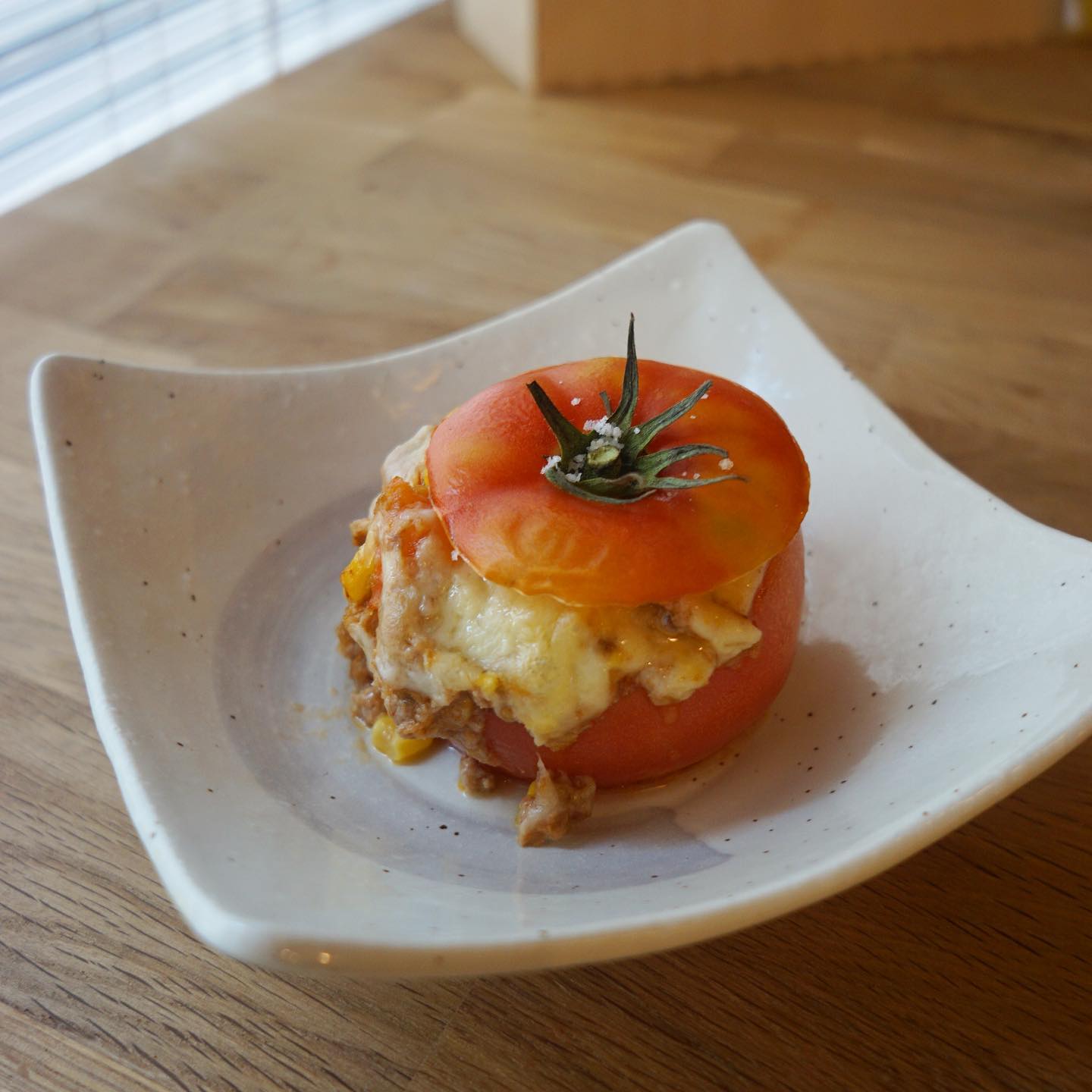 8月は何かとお休みをたくさんいただき、申し訳ないですね！でもその分勉強して、新メニュー繰り出しますよ〜！
まずは「丸ごとトマトのファルシー」南仏の郷土料理、家庭料理です。トマトをくり抜いた中にひき肉餡を詰めてチーズを乗せて焼くだけ！　くり抜いたトマトとトウモロコシをひき肉と一緒に炒めて、夏らしく仕上げました。トマトのグラタン！って感じで素朴に美味しいです。おひとついかが〜？（麻）