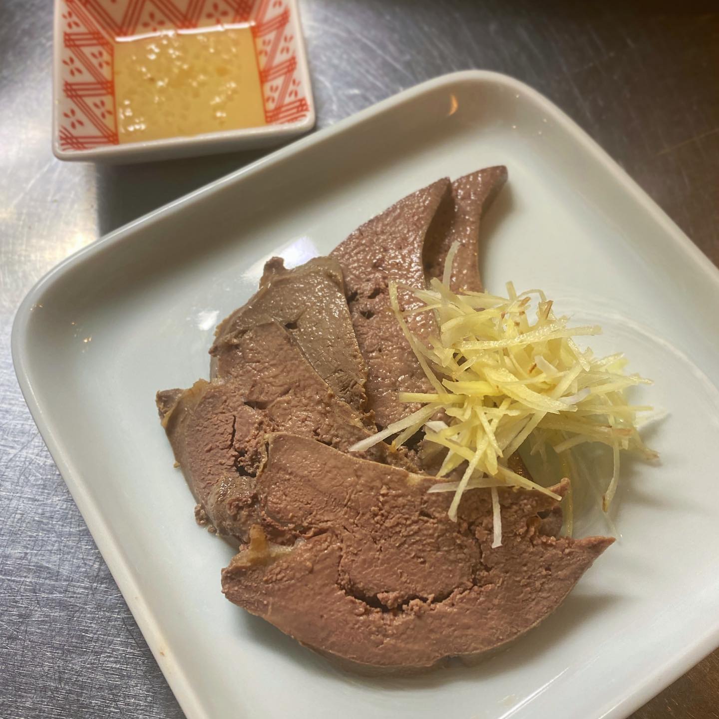 豚のレバーはお好きですか？
嫌いな方はホント苦手！という方も多いかと思いますが、、店長ミヤザキはこの手のものが大好きなんですよ。レバニラ炒めがあったら頼む派です。で、こちらは「豚レバーの冷菜」です。新鮮な豚のレバーを血抜きしてから香味野菜たっぷりの煮汁でコトコト煮てそのまま煮浸しに。針生姜と針ニンニク？！の薬味を添えていただく、ほんのり中華風の冷菜です。昔「壇流クッキング」を読んで、家でたまに作っていたのを急に思い出し、食べたくなって作ってみました。いかがですかー？（麻）