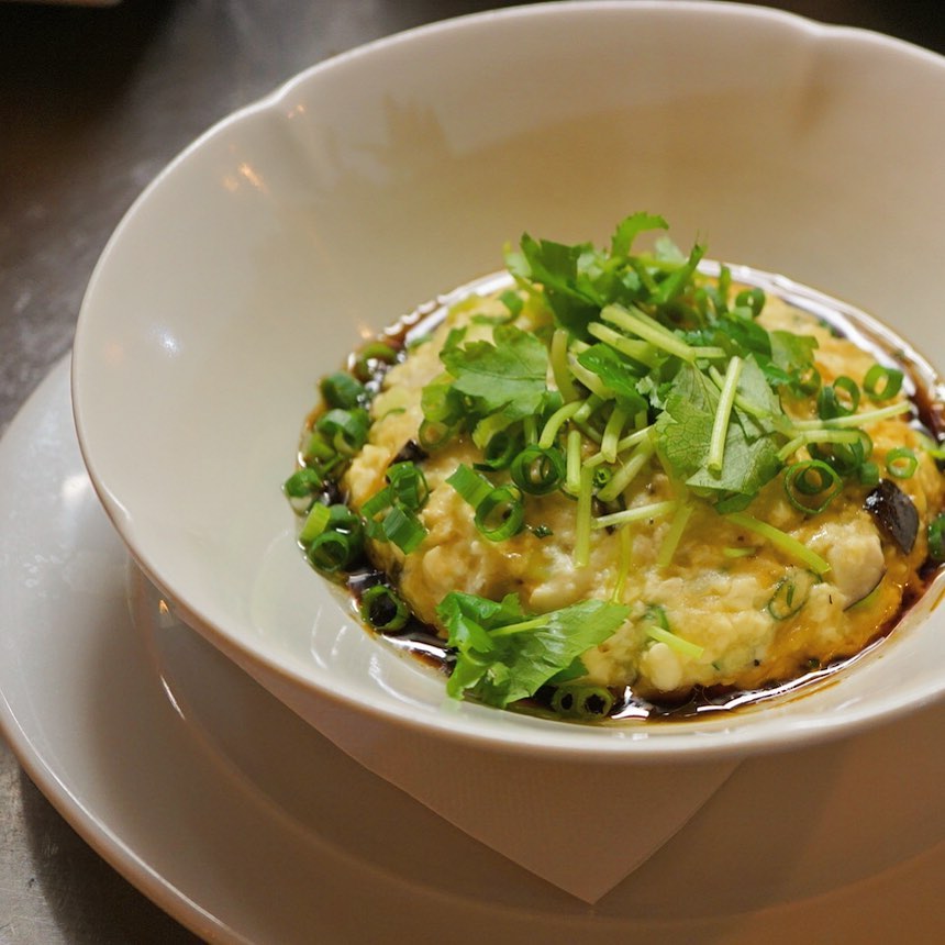 ひさびさの、ホタテ入り蒸し豆腐をご用意しましたよ！干し椎茸と帆立貝柱の旨味たっぷりの蒸し豆腐。仕上げに三つ葉と醤油とごま油で、ほんのり中華風？熱々のうちに食べるが吉！お持ち帰りはできませんのでよろしくお願いします。（麻）