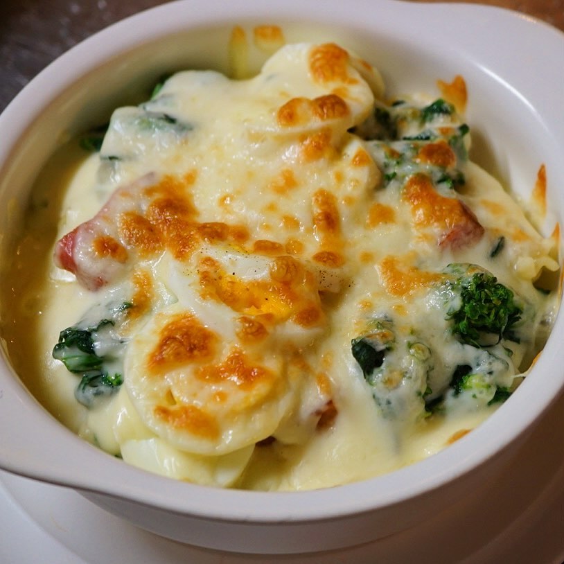 さてとあつあつメニューのグラタンもちょっぴり春の味覚です！「菜の花とベーコン、ゆで玉子のマカロニグラタン」！ほろ苦菜の花のみどりと旨みのベーコンは赤、ゆで玉子の黄色を加えて春のトリコロール！色味もすてきな春のグラタン！（お）