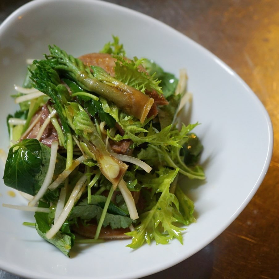 先週末から夜の冷菜メニューでお出ししております、牛タンと山菜・香味野菜の冷製！新メニューですよ。柔らかくなるまでじっくり煮込んだ牛タンを薄くスライスして、ウドや三つ葉、わさび菜など香り高い野菜と一緒にサラダ仕立ての冷製に。タラの芽もちょいとのせて春の香り、のせのせで。
みんな大好き、にんにくレモンドレッシングで和えたら、日本酒からワイン、ビールまで守備範囲の広いおつまみになりました。ぜひお試しあれ！（麻）