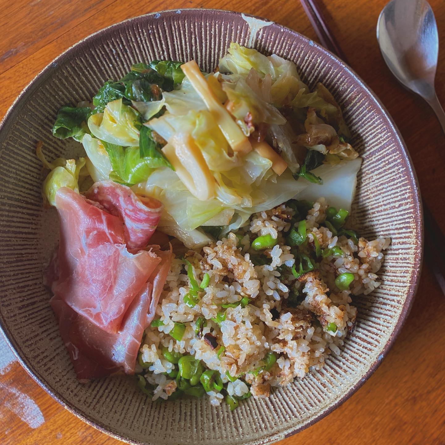 野菜をいっぱい食べよう！とご飯少なめシシトウと昨日の残りの枝豆たっぷりチャーハン。キャベツとメンマとレタスの外っ葉という冷蔵庫の残り物を胡麻油とニンニクで元気に蒸し炒め。お肉の要素何にも無しで、ちょいとだけ今日の夜つまみ用に、昨日シミシエッダで買っておいた生ハムと燻製サラミを添えて。